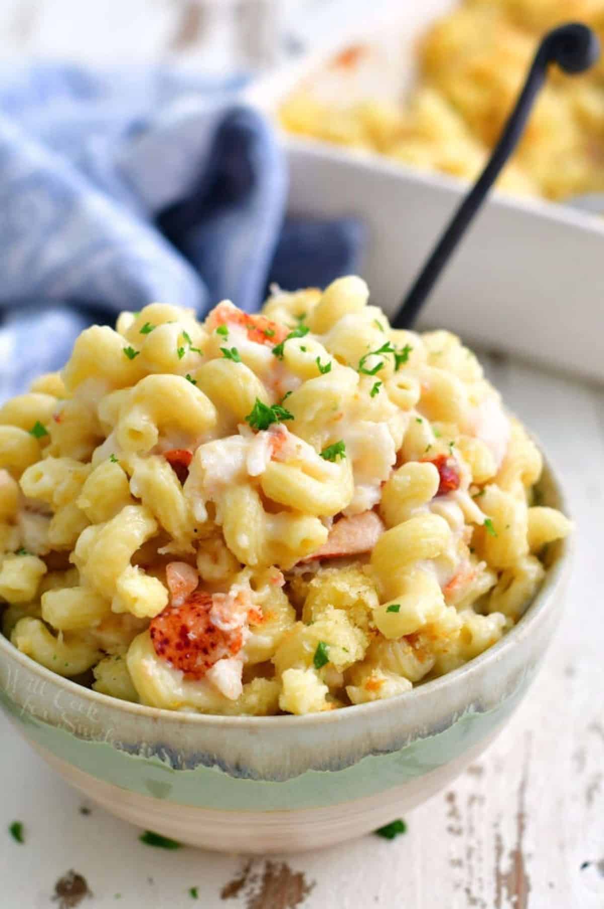 a bowl full of lobster mac and cheese with corkscrew pasta and a fork.