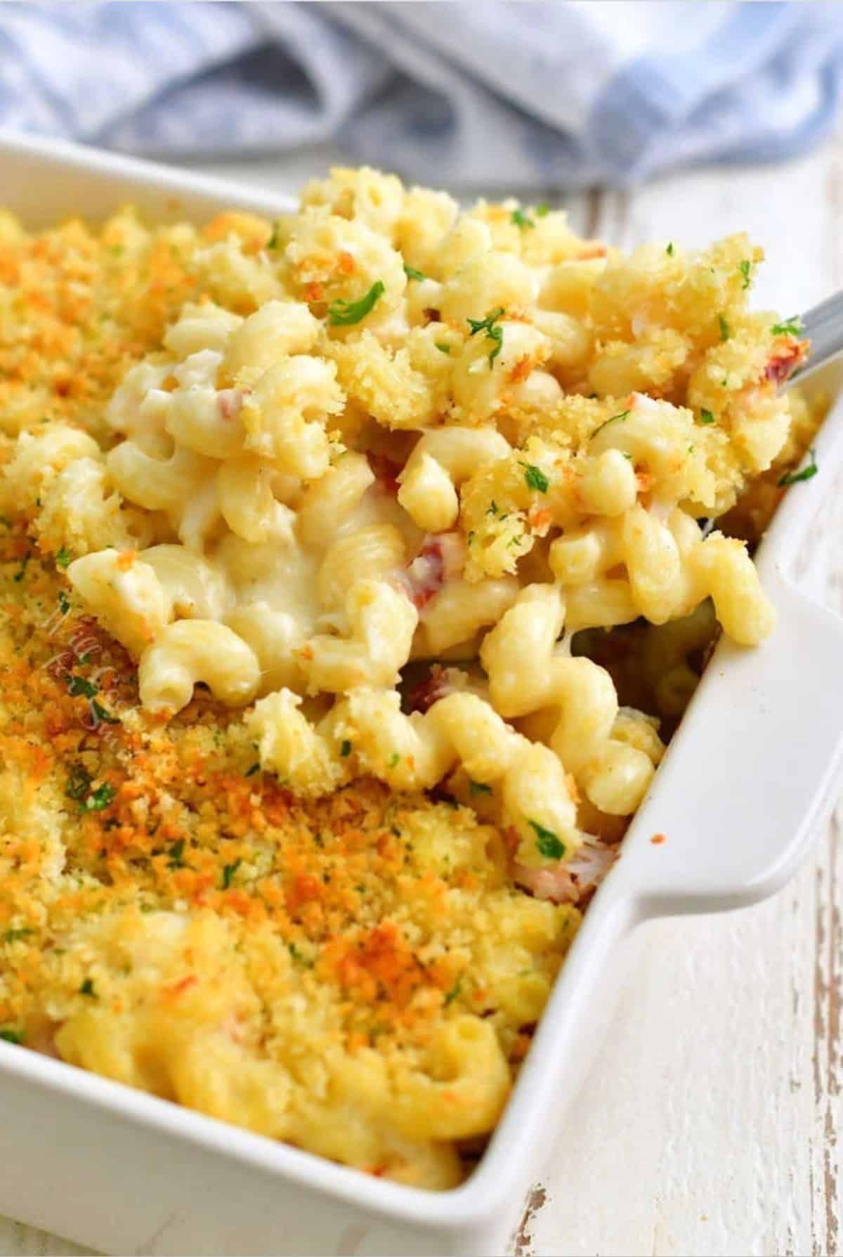 scooping out some mac and cheese from a baking pan with a ladle.