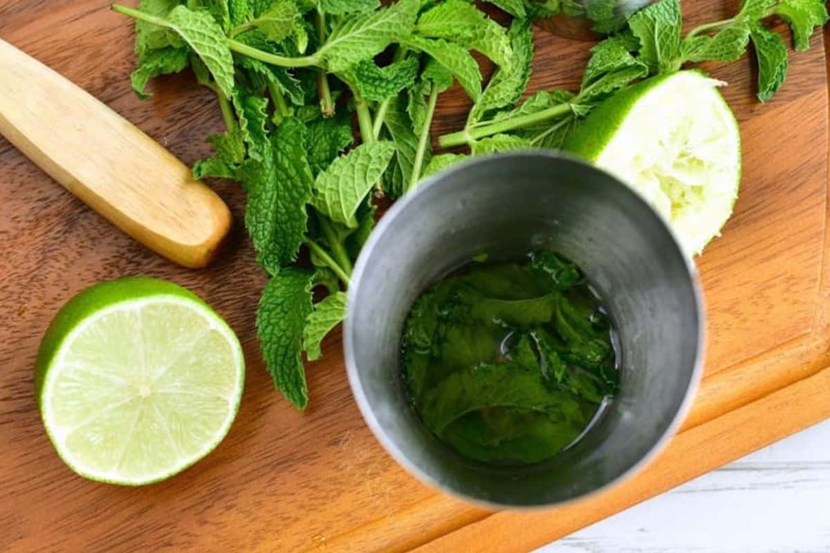 muddled mint with lime juice and simple syrup in the cocktail shaker and limes and mint around.