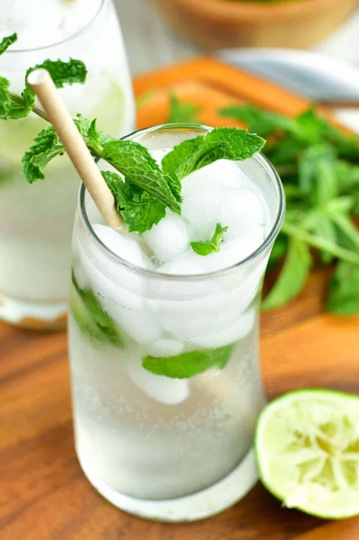 clear mojito cocktail in a curved glass with mint and a paper straw.