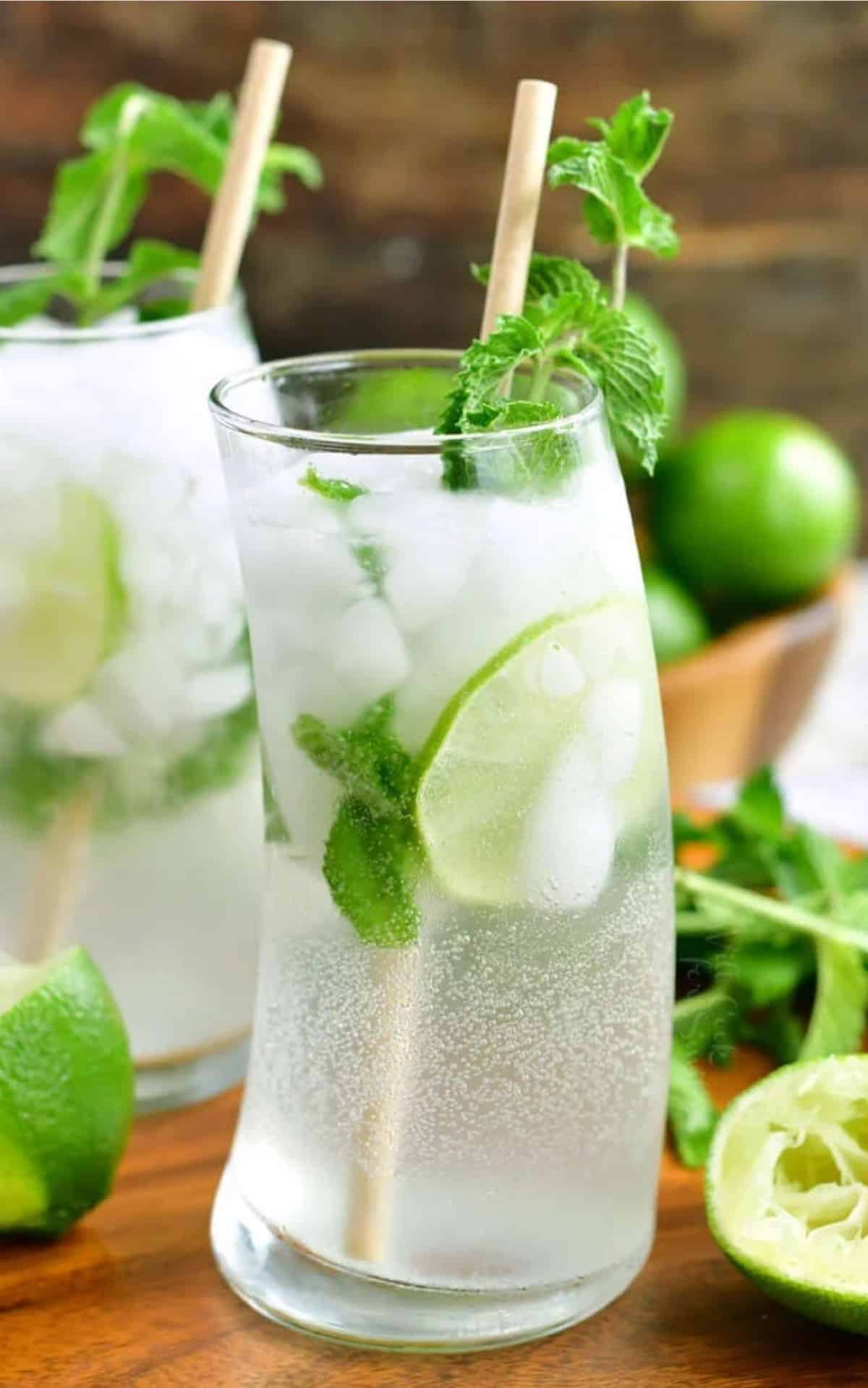 tall curvy glass of mojito and limes and mint on the background.