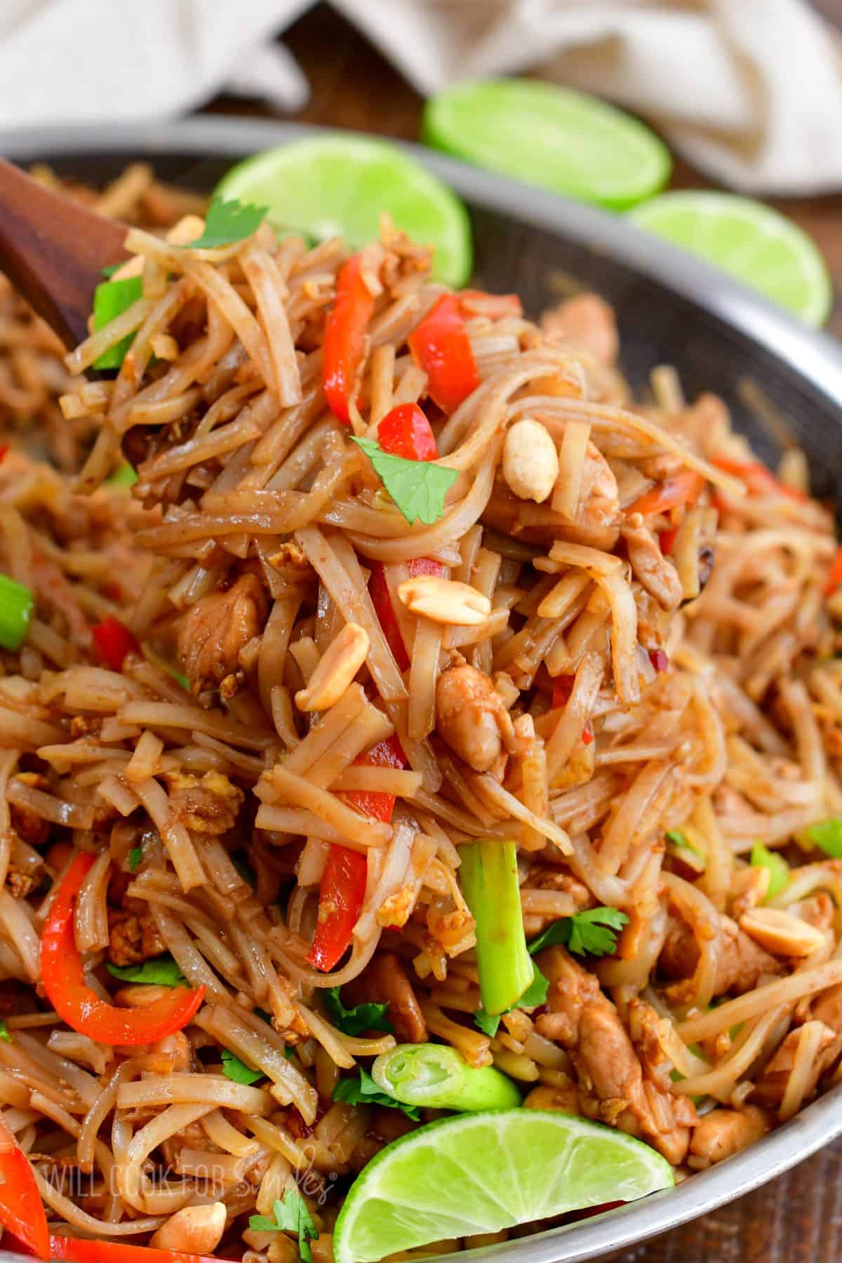 A large spoon is holding a portion of pad thai over the skillet. 