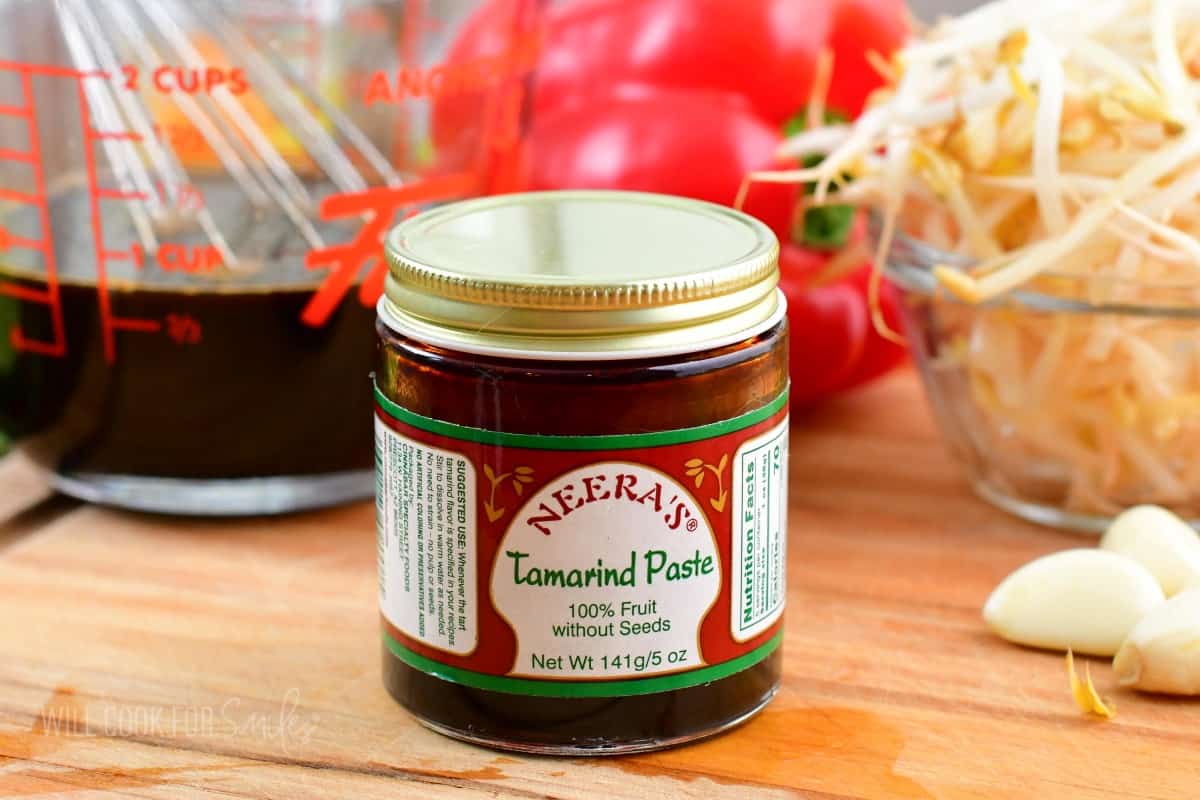 tamarind paste in a small jar on a cutting board with veggies and sauce around.