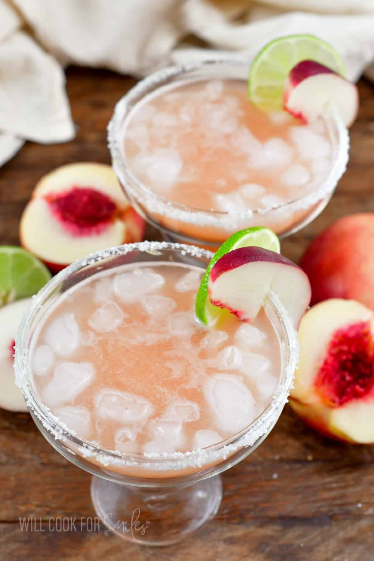 two margarita glasses filled with peach margarita mixture and ice.