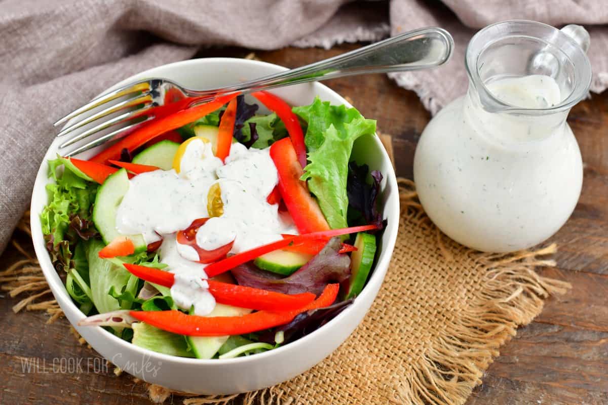 a small green salad with some ranch dressing on top and some dressing in a glass jar.