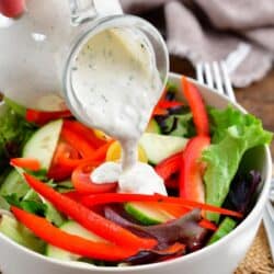 pouring ranch dressings over a green salad with peppers and cucumber.