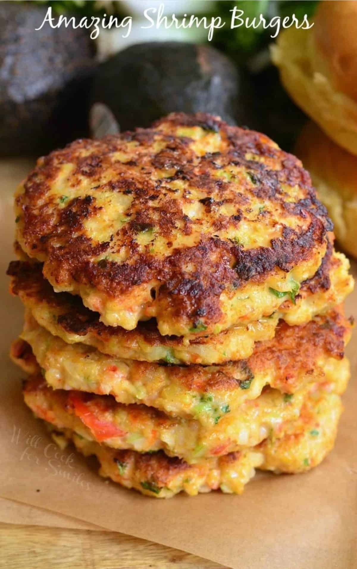 a stack of several shrimp burgers on top of parchment paper with avocado next to it.