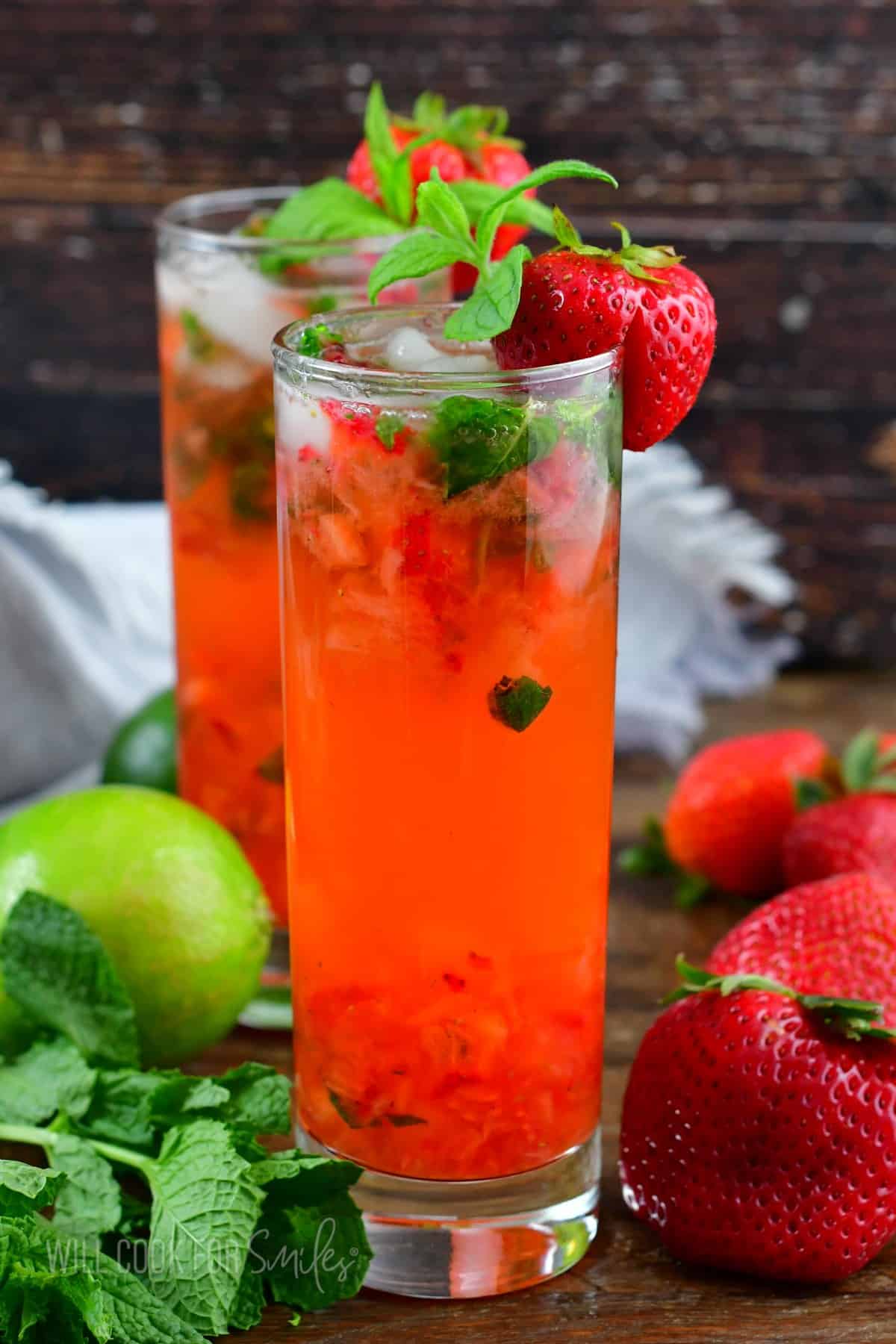 tall glass with bright pink strawberry cocktail with mint and strawberries around.