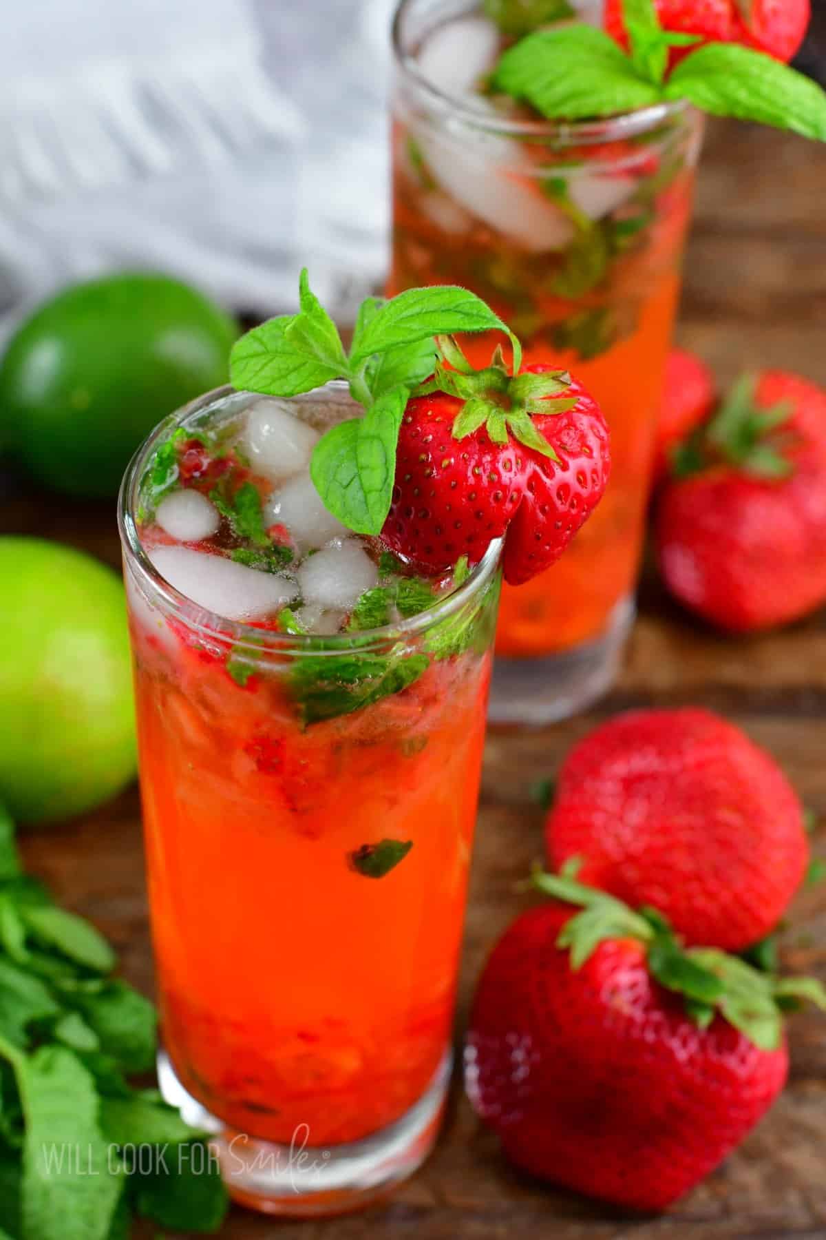 two glasses with bright strawberry mojito cocktails and berries around on the table.