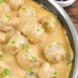 several meatballs in creamy gravy in the pan with a metal spoon.