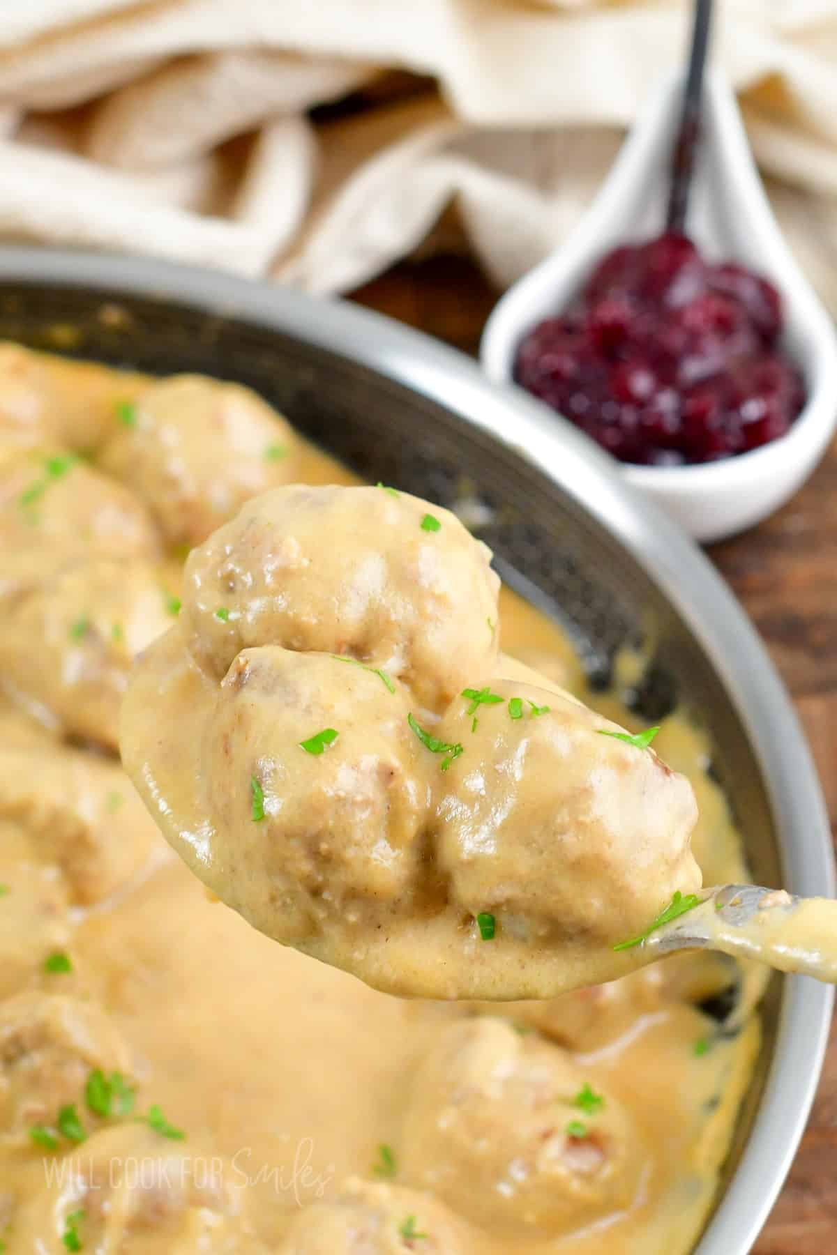 A spoon has lifted some swedish meatballs from the skillet. 