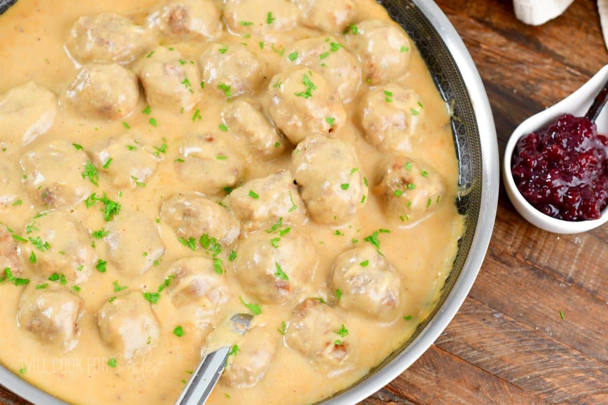 A pan filled with meatballs and gravy is placed next to a small serving dish of jam. 