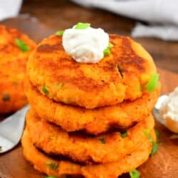 A stack of sweet potato cakes on a cutting board with a dollop of sour cream on top with green onions.