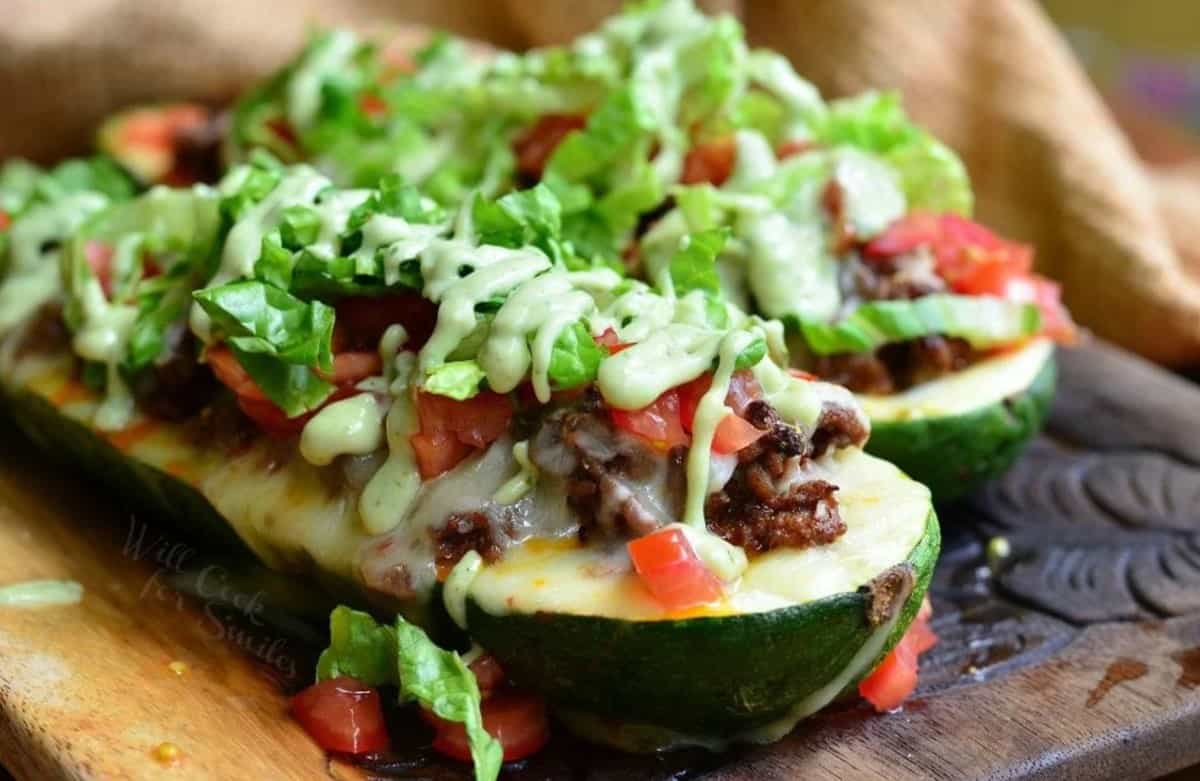Two garnished zucchini boats are placed on a wooden surface. 
