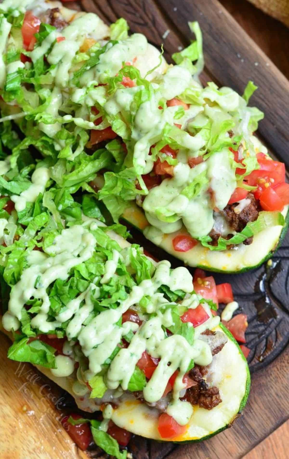 Two taco zucchini boats are placed on a wooden surface. 