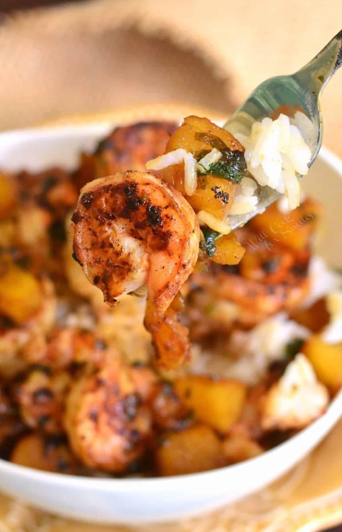 holding a fork with some shrimp and pineapple on it over the rice bowl.