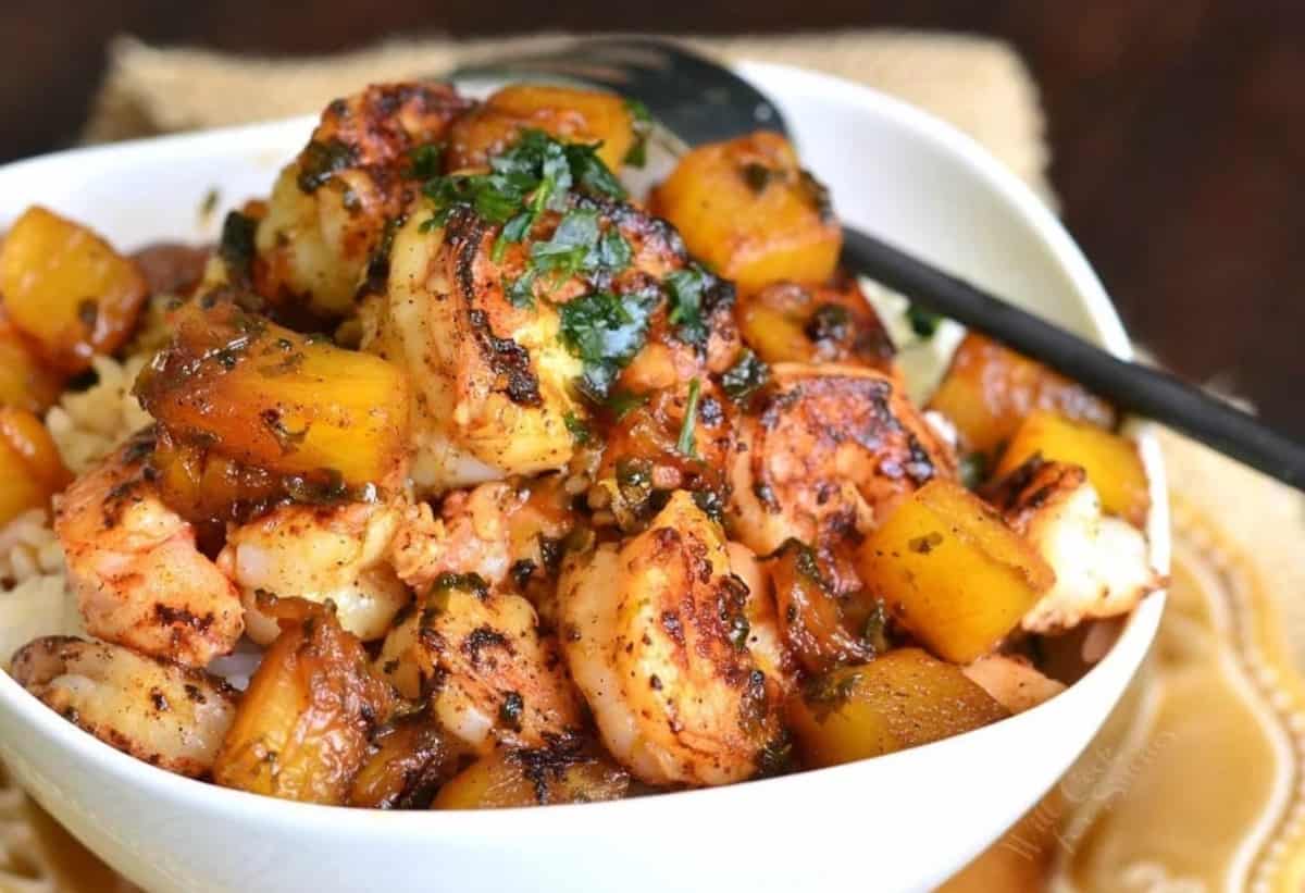 Cilantro garnishes over seared shrimp and pineapple over rice in a bowl.