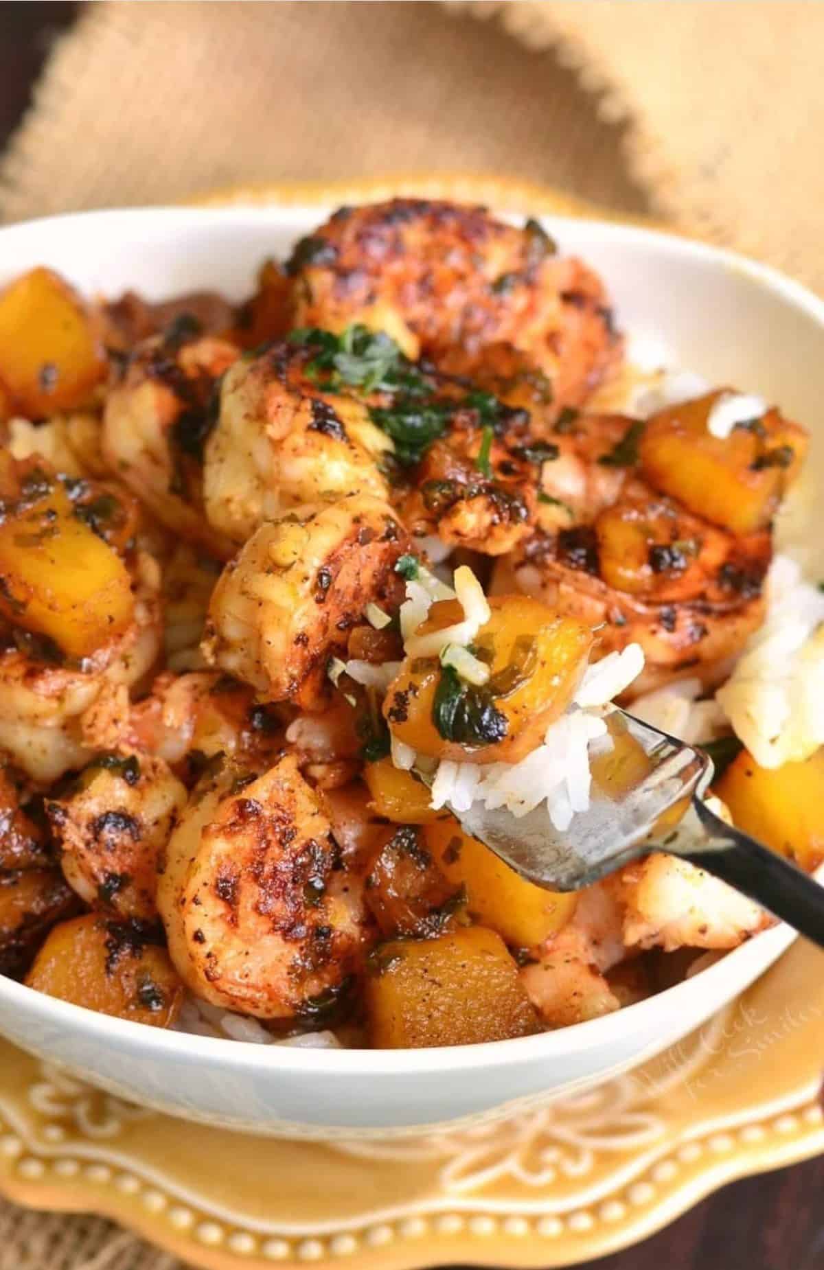 A fork is lifting a bite of rice and shrimp from a full bowl. 