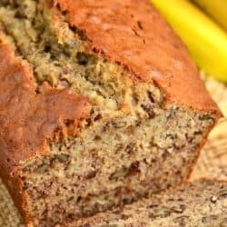 banana bread with a slice out of it laying on a burlap placemat.