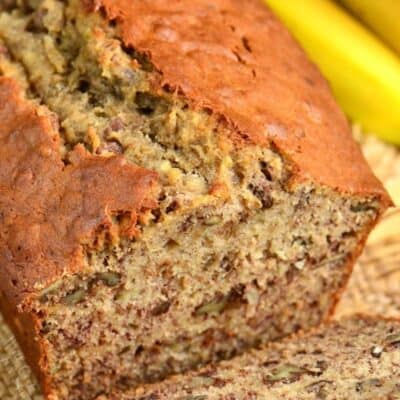 banana bread with a slice out of it laying on a burlap placemat.