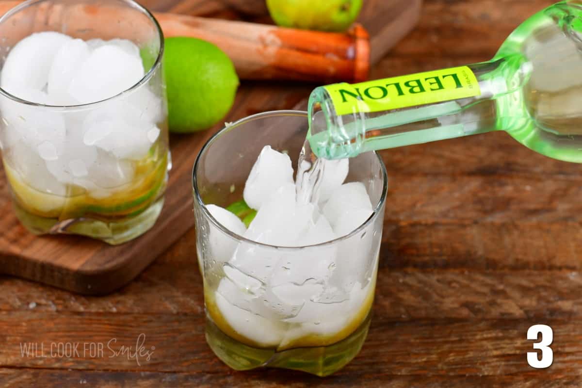 pouring Cachaca into a short glass with ice on a wood surface.