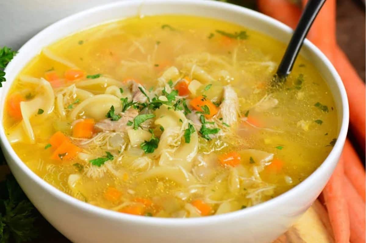 A bowl of chicken noodle soup with a spoon in the bowl.