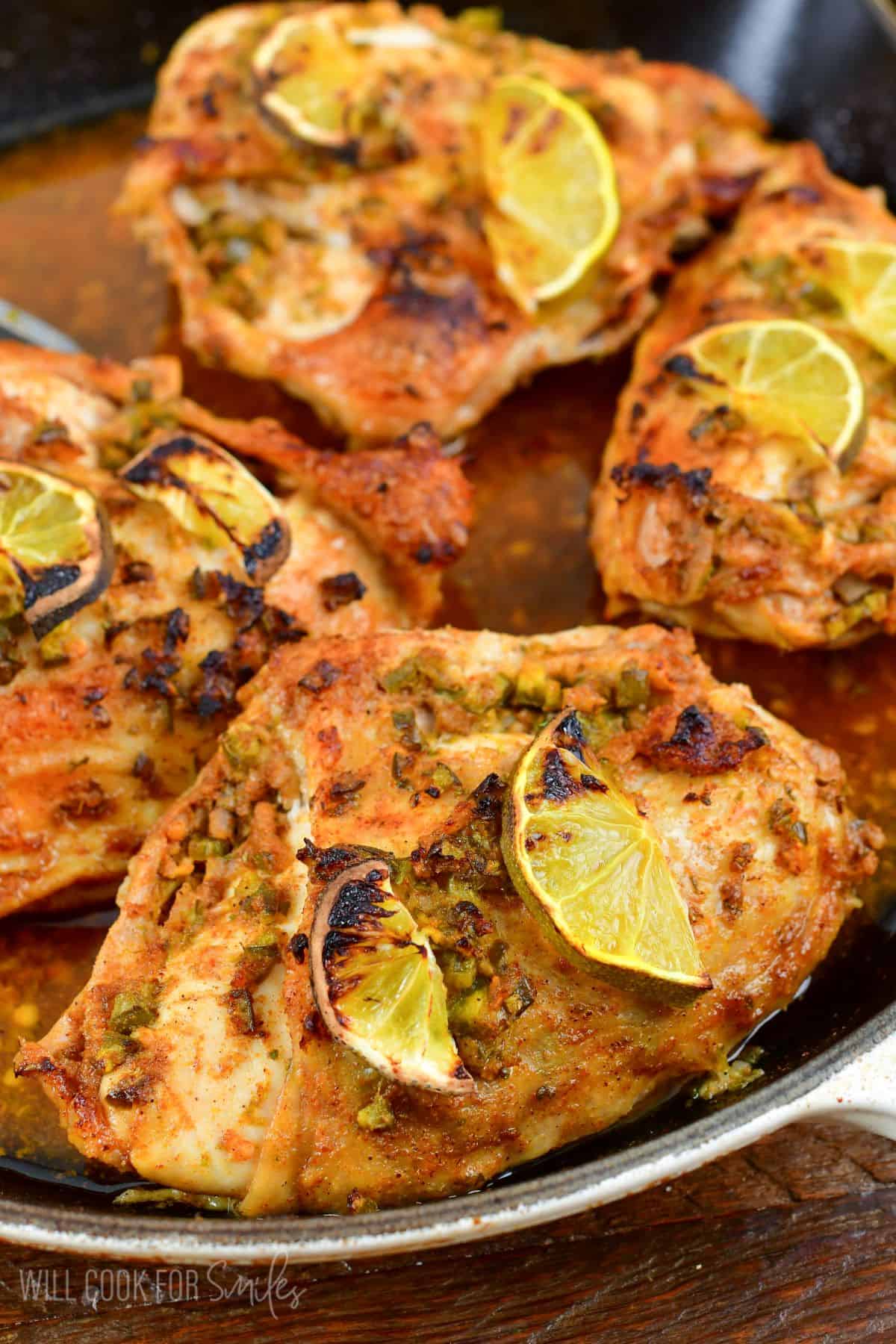 Four pieces of chicken in a pan with lemon slices on top.