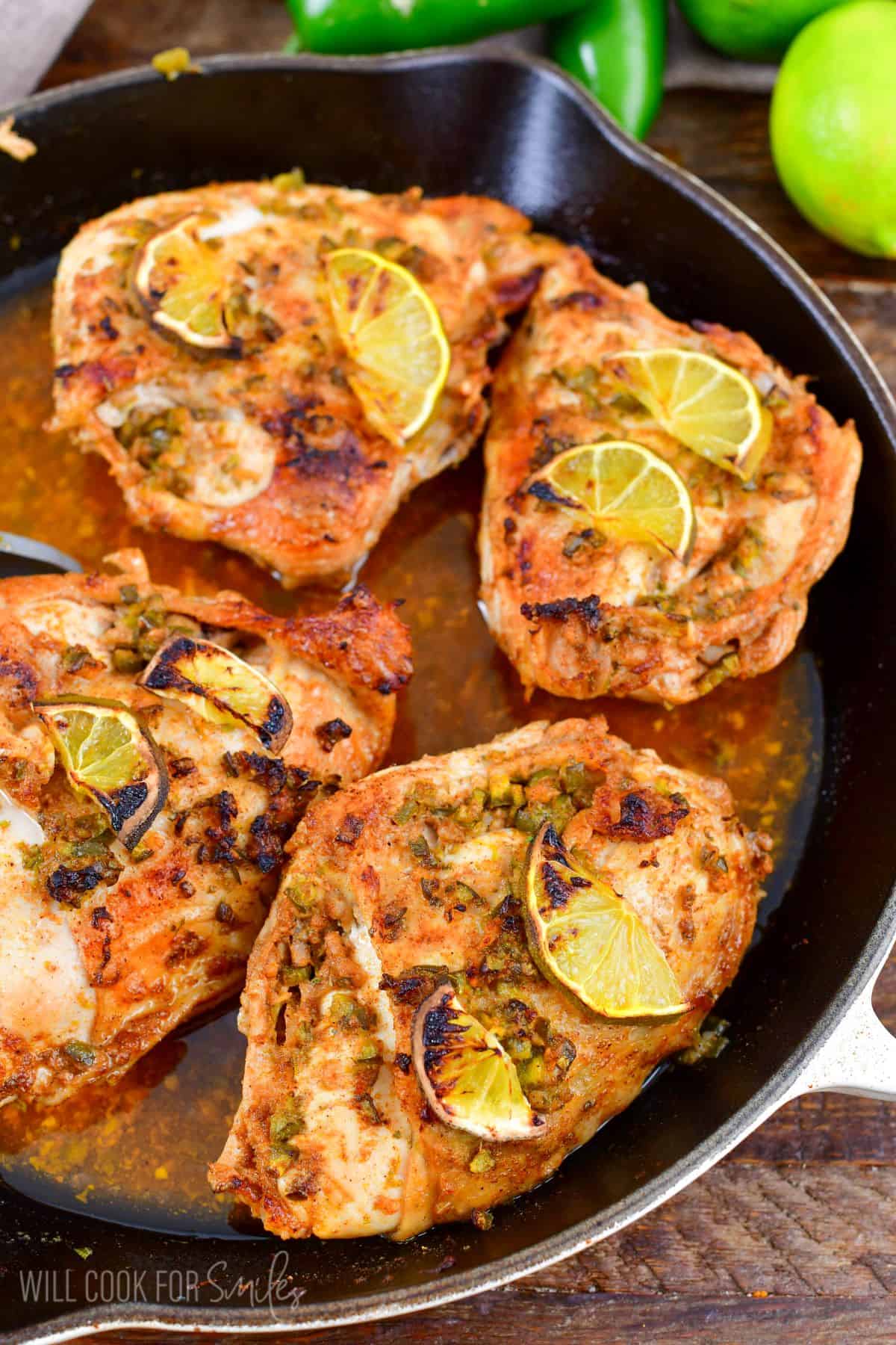 Charred pieces of lemon are placed on top of chicken breasts in a skillet. 