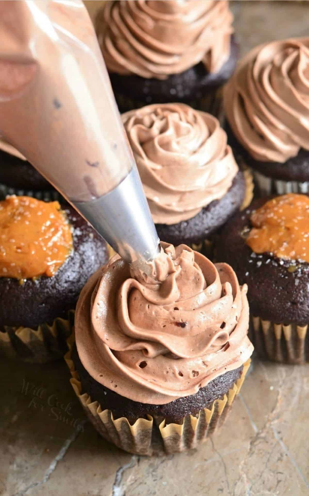 piping chocolate frosting onto a cupcake out of the piping bag and metal tip.