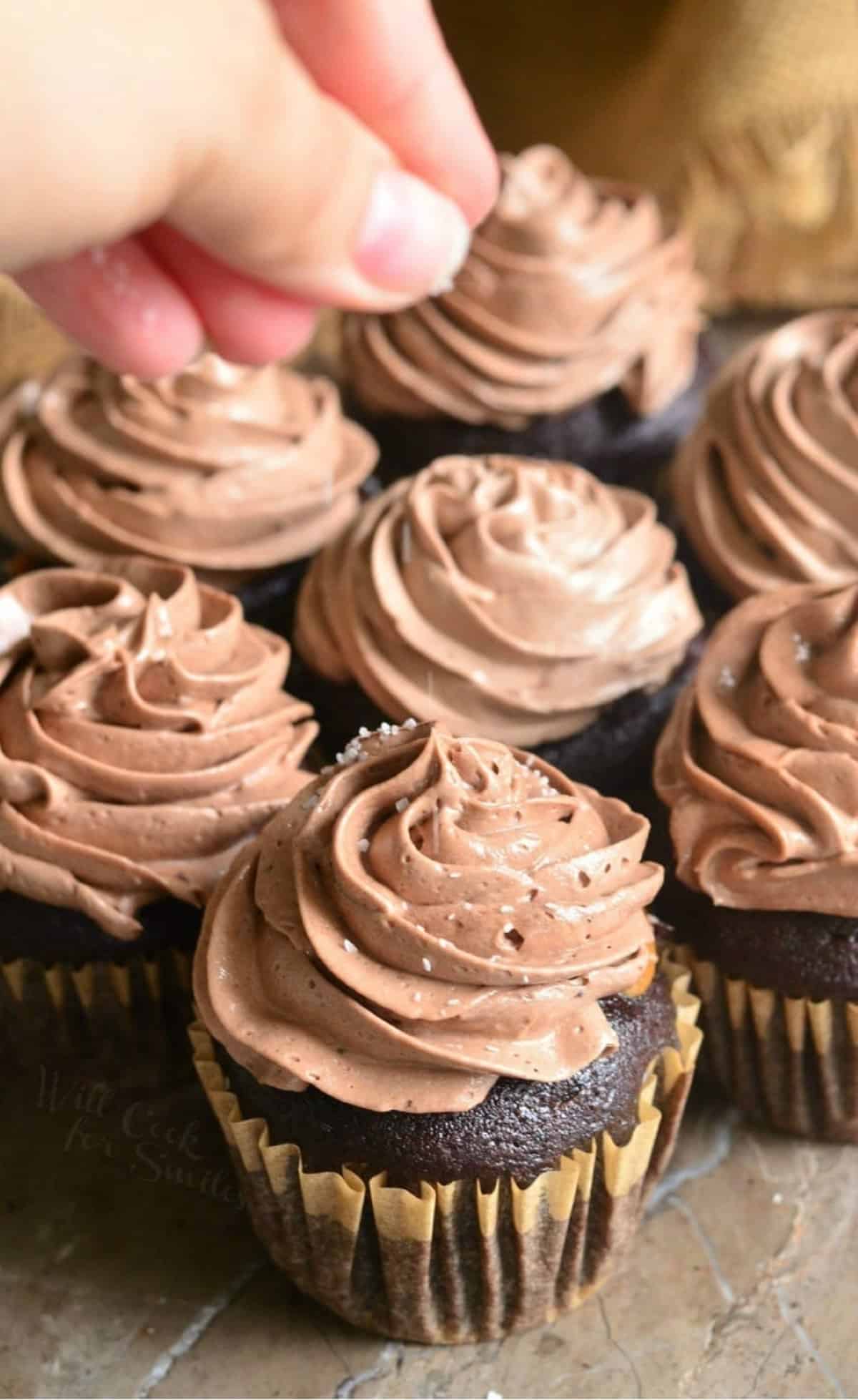 adding sprinkle of coarse salt on top of chocolate frosting on the cupcakes.