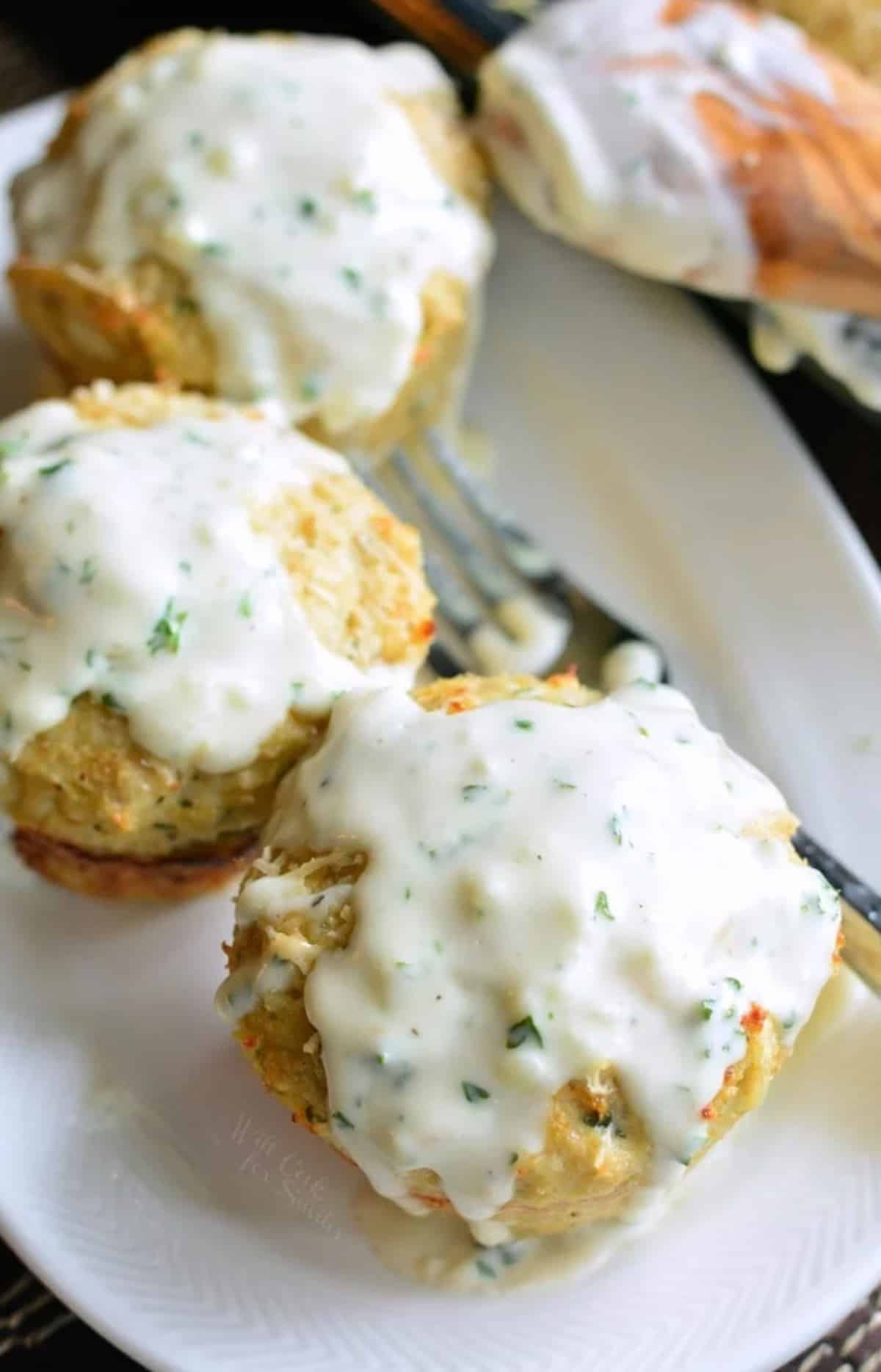 three mini chicken meatloaves with cream sauce on top on a long plate.