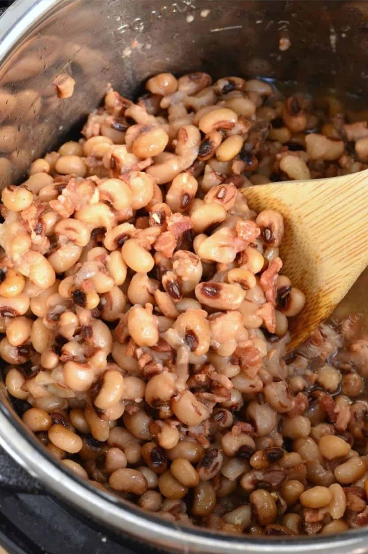 black eyed peas in the instant pot with a wood spoon stirring beans.