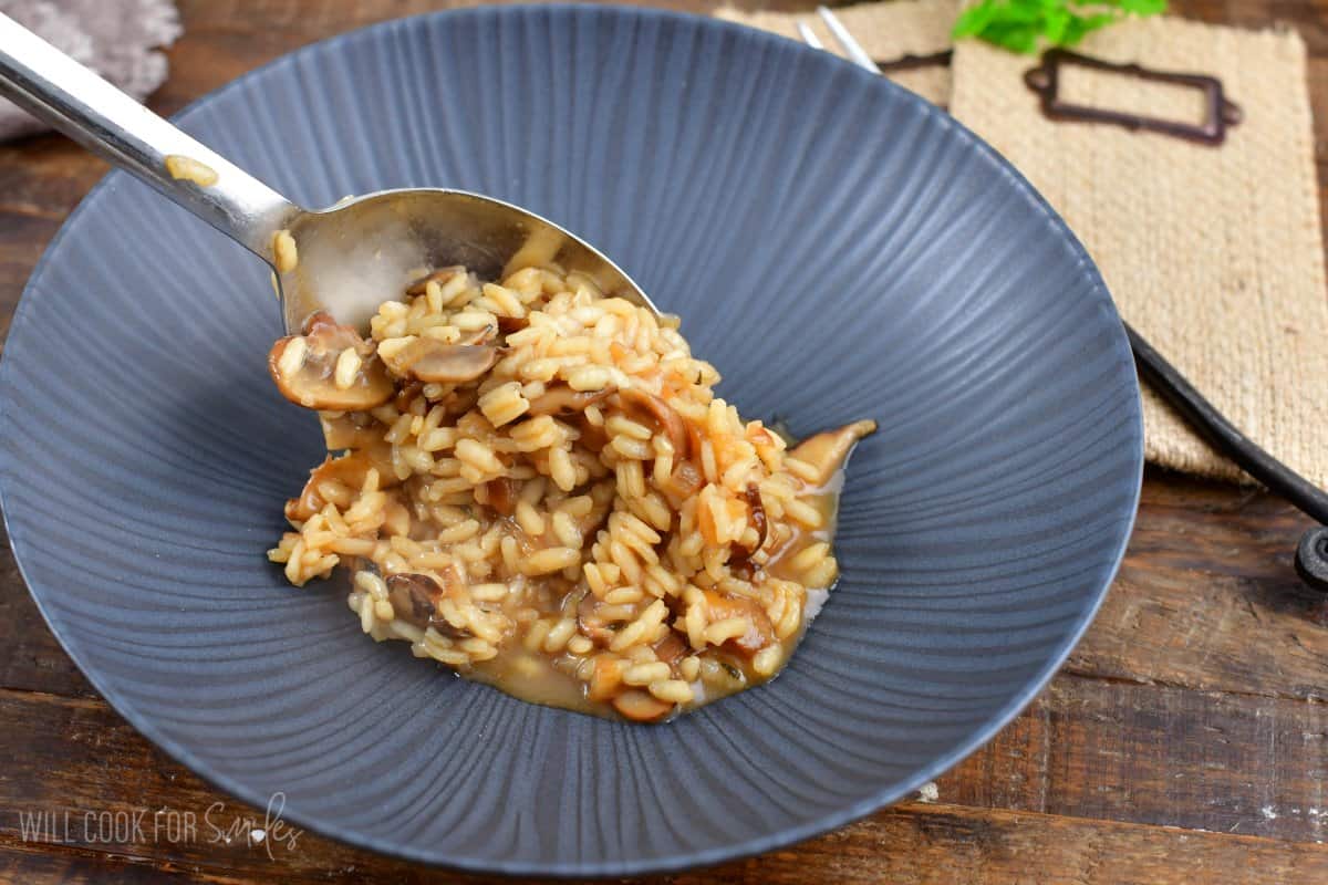 scooping risotto with a big spoon into a wide bowl.