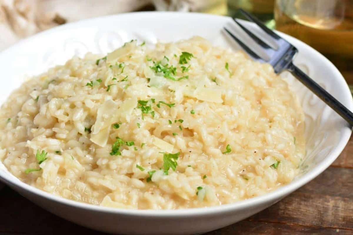 parmesan risotto in a bowl with parsley and cheese as garnish on top and a fork to the right.