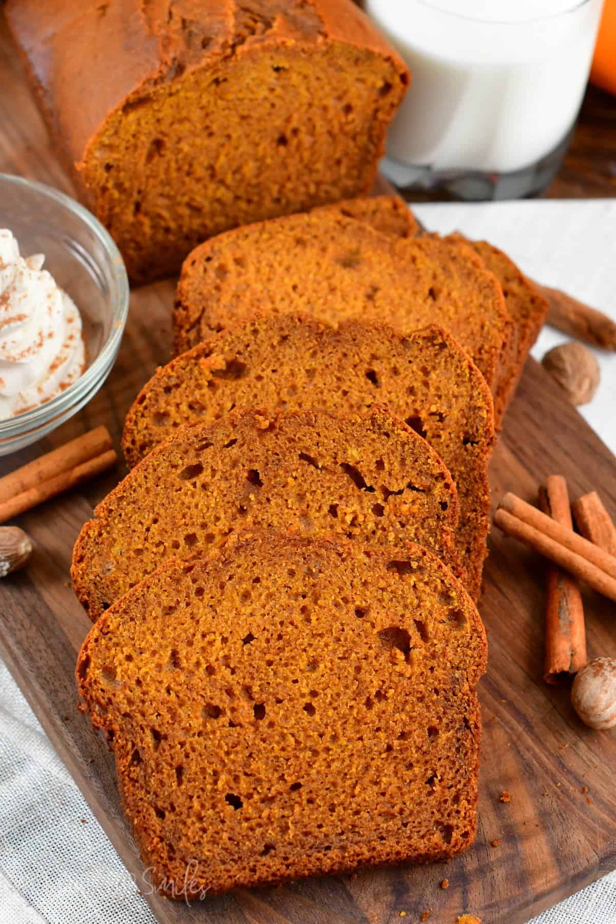slices of pumpkin bread on a wood surface with cinnamon sticks next to it.