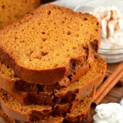 pumpkin bread slices stacked up and whipped cream on a spoon next to it.