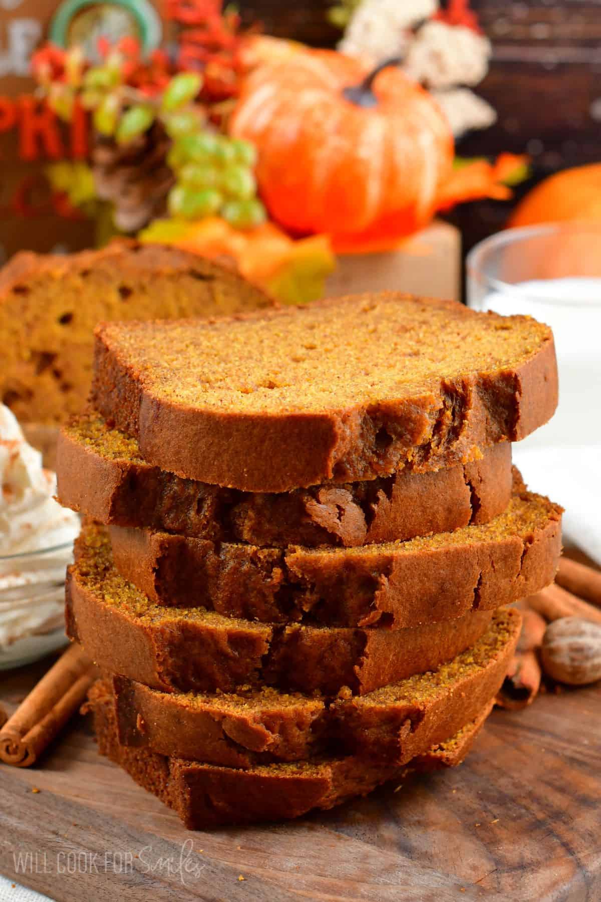 pumpkin bread stacked up on a wood surface with cinnamon sticks.