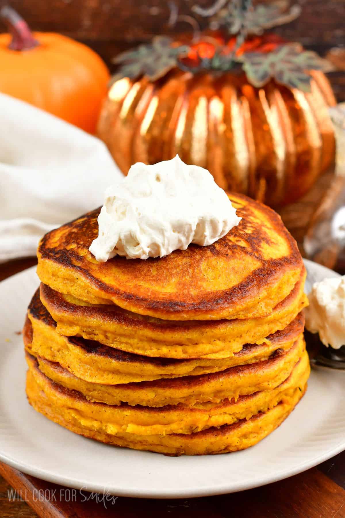 A stack of pumpkin pancakes on a plate with whip cream on top.