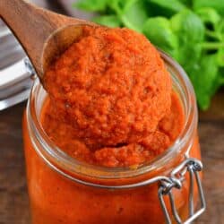 spaghetti sauce in a glass jar on a wooden surface with a wooden spoon lifting some out.