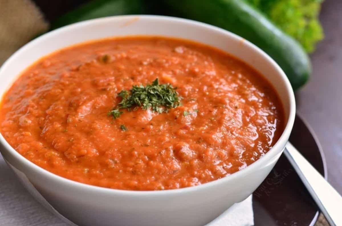 Tomato Zucchini soup in a white bowl with fresh basil and garnish on top.