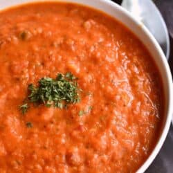 Tomato zucchini soup in a white bowl with a spoon to the side.