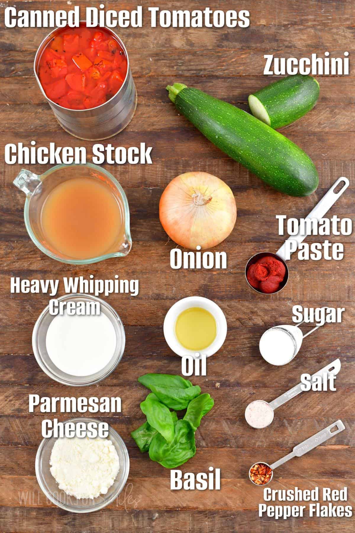 The ingredients for zucchini tomato soup labeled and placed on a wooden surface.