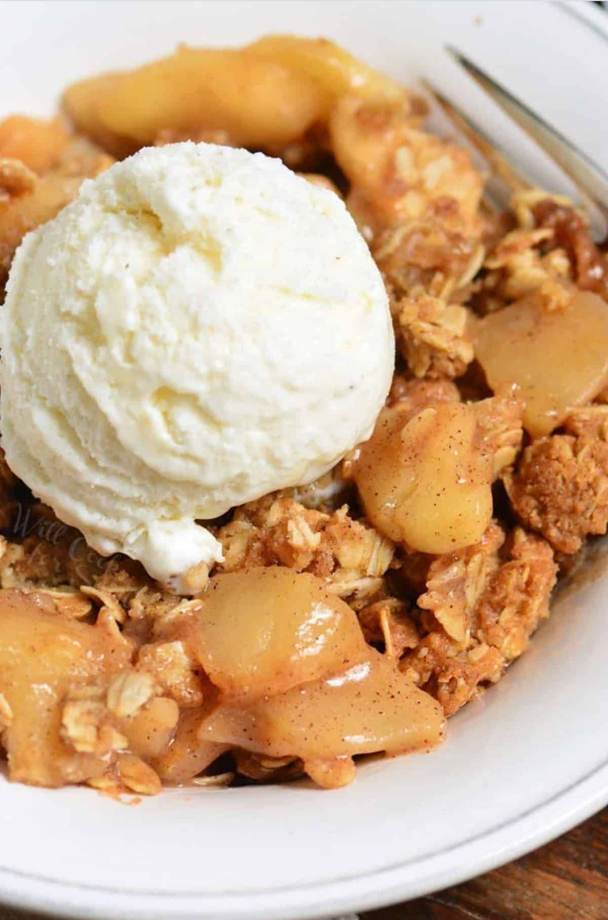 apple crisp with a scoop of vanilla ice cream on top in a white bowl.