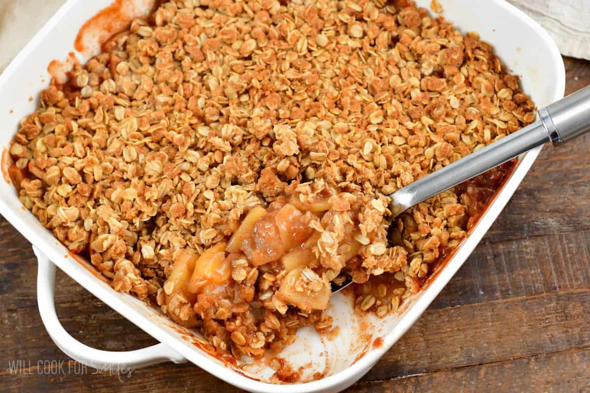 apple crisp in a baking dish with a spoon in the baking dish and scoop taken out.