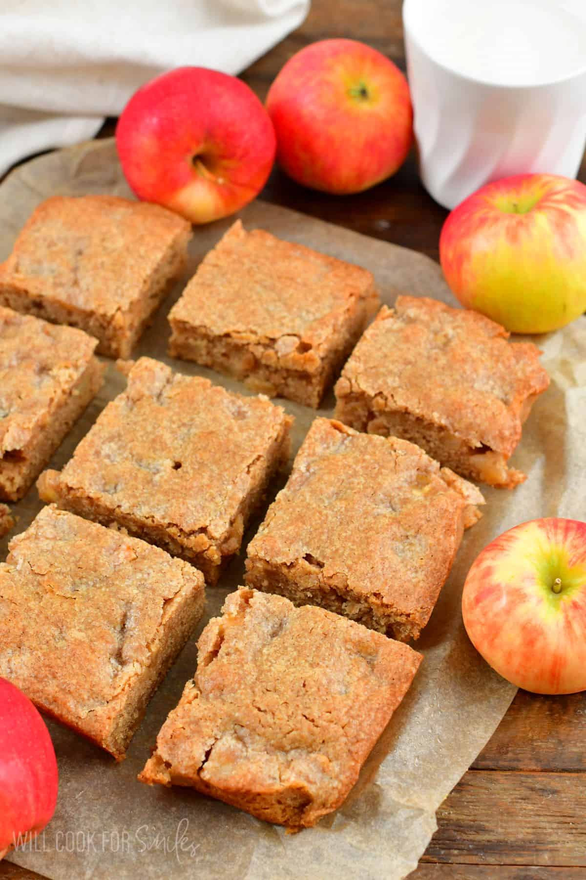Apple pie blondies cut up on parchment paper with apples around them.