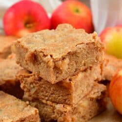 Apple pie blondies stacked up on wax paper with apples in the background.