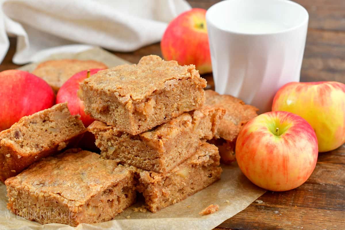 apple pie blondies sliced and stacked up on wax paper with apples around them.