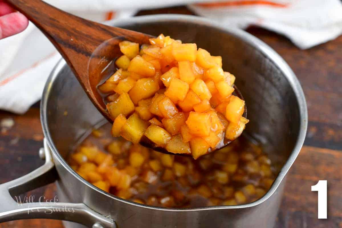 holding a large wooden spoon full of apple pie topping.