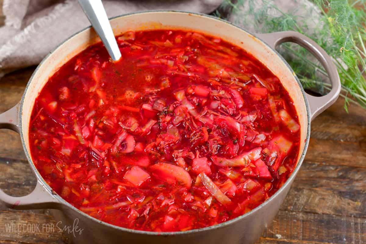 Borscht in a pot with a metal spoon on a wood surface.