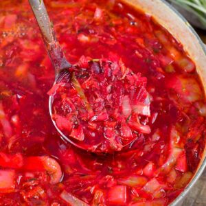 borscht soup in a pot with a ladle scoop of soup being lifted out.